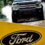 Used Ford trucks are good used for mudding and off-roading, a black F-150 is shown on a dirt track from the front behind a yellow Ford flag.