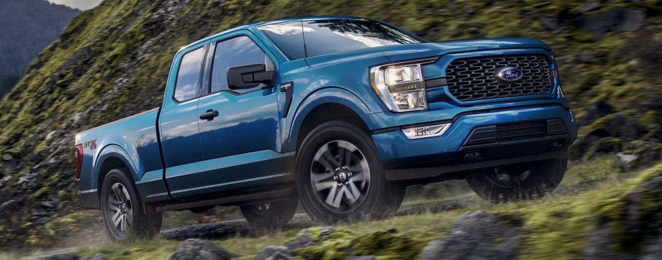 A blue 2021 Ford F-150 is off-roading on a trail in Albany, NY.