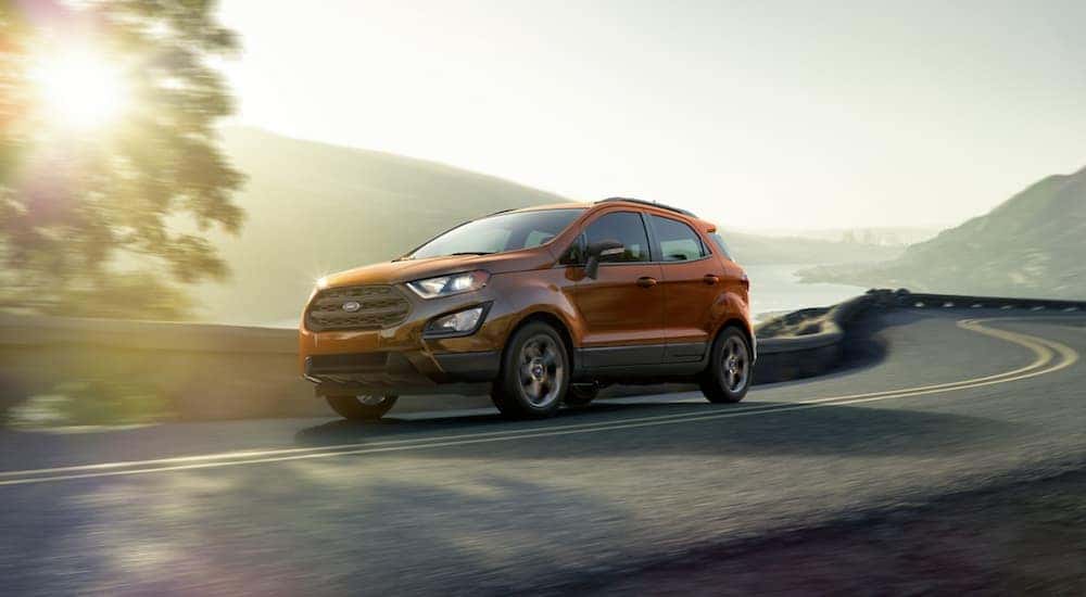 An orange 2020 Ford EcoSport SES, which is popular among Ford SUVs, is driving past hills at sunset near Albany, NY.