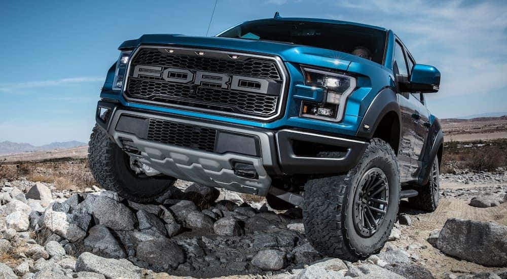A blue 2020 Ford F-150 Raptor is off-roading on rocks, and will be a popular trim on the Ford trucks in 2021.