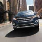 A blue used 2017 Ford Edge is driving through a city and shown from the front.