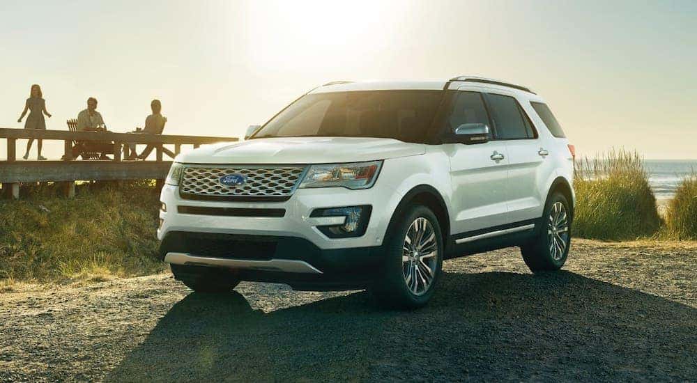 A white 2017 Ford Explorer Platinum is parked at a beach in front of a boardwalk and the sun.