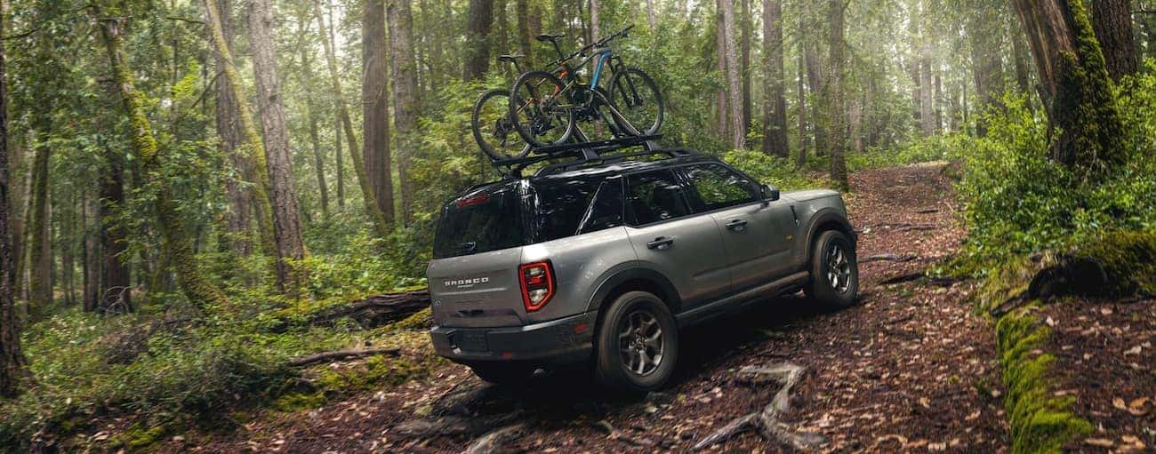 A grey 2021 Ford Bronco Sport is off-roading in the woods with bikes on the roof.