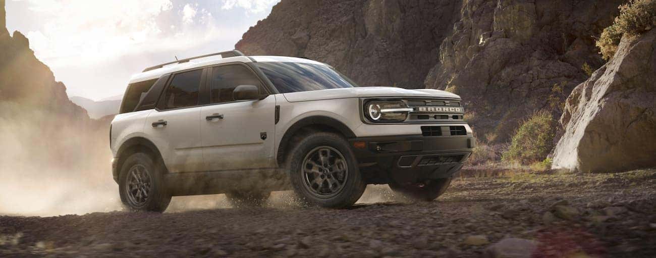 A white 2021 Ford Bronco Sport is kicking up dust while off-roading in front of rocky hills.