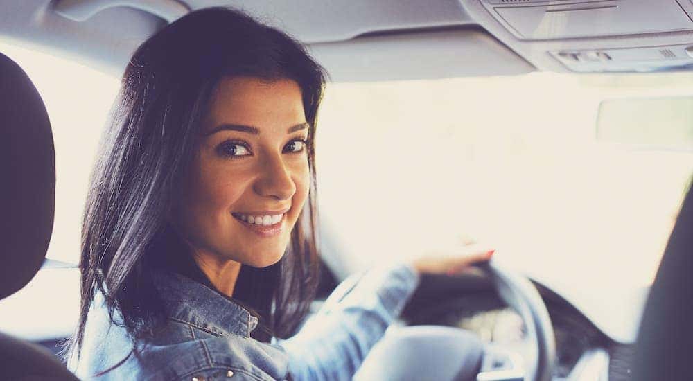 A smiling young woman is sitting in a car and looking into the back seat at the camera.