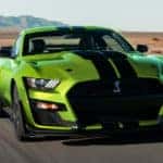 Lime green and black 2020 Ford Mustang sports car driving on a pave road with mountains in the background