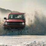 A red 2021 Ford Bronco is driving through waves on the beach after leaving a Ford dealership.