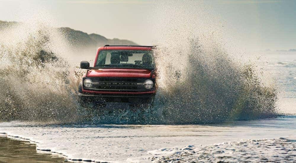 A red 2021 Ford Bronco is driving through waves on the beach after leaving a Ford dealership.