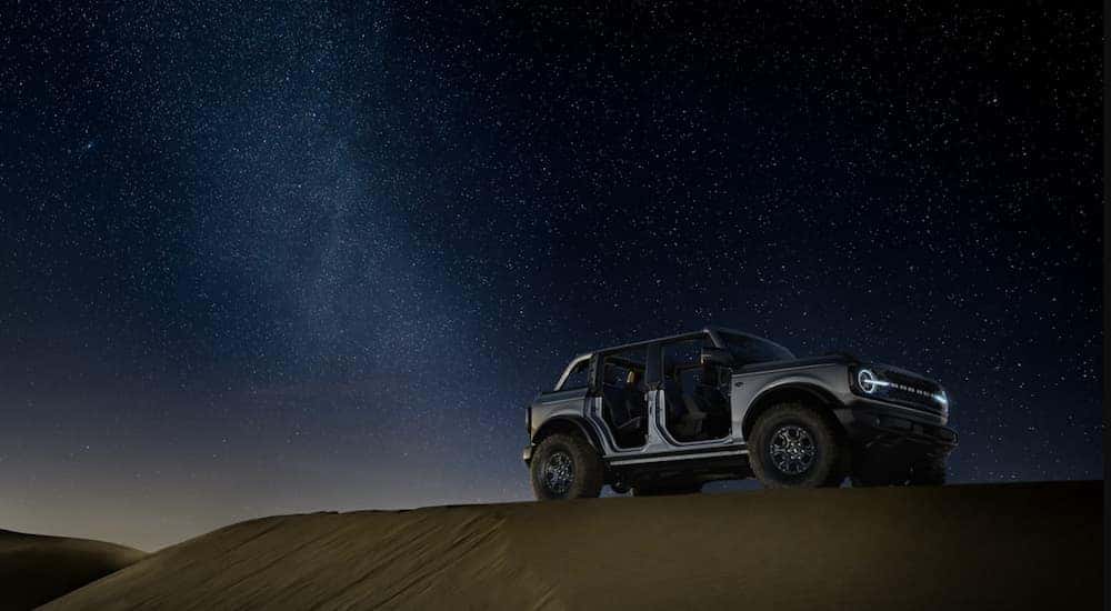 A grey four-door 2021 Ford Bronco is parked under a starry sky with no doors.