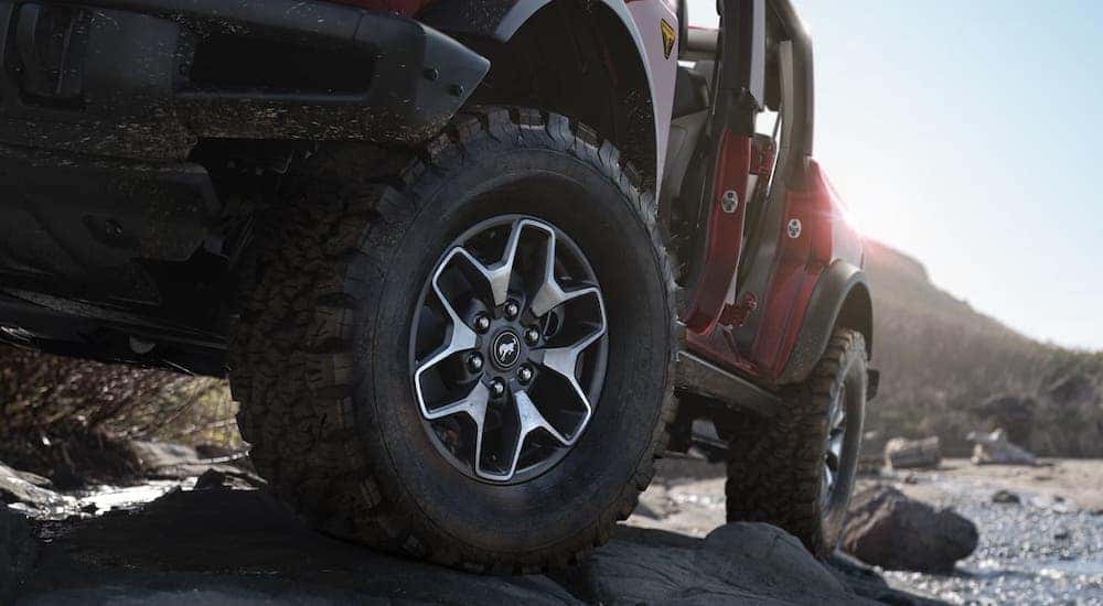 A closeup shows the wheel of a red 2021 Ford Bronco Badlands 4-door that is climbing over rocks near Albany, NY.