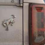 A closeup shows the badging on the back of a white 2021 Ford Bronco that is covered in mud.