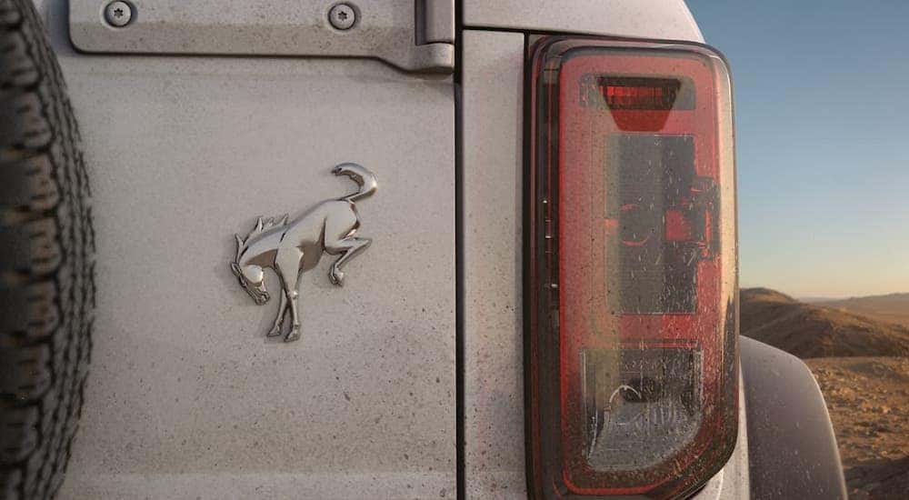 A closeup shows the badging on the back of a white 2021 Ford Bronco that is covered in mud.