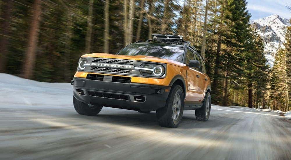 A new Ford SUV hitting the roads, an orange 2021 Ford Bronco Sport, is shown driving on a woodland road.