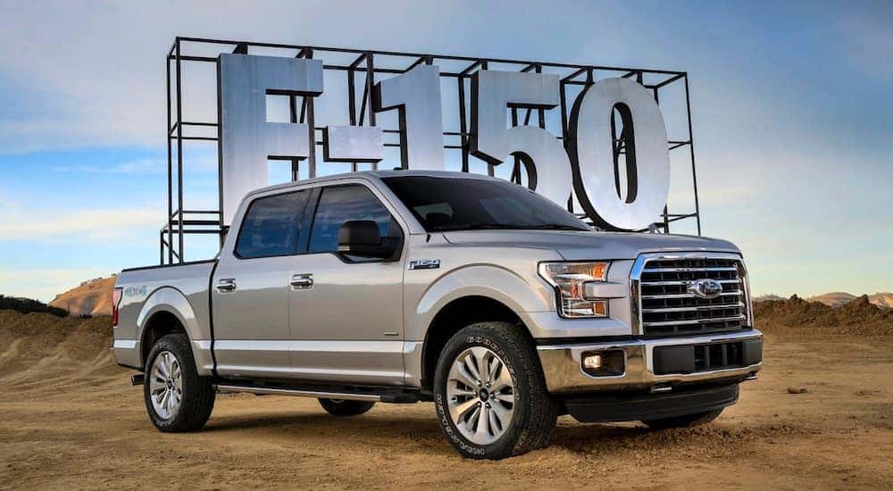 Silver Ford F-150 parked on dirt in front of a silver sign that says "F-150"