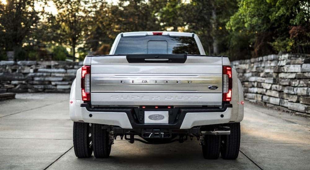 Back view of a white 2018 Ford Super Duty truck parked in a driveway next to a stone wall