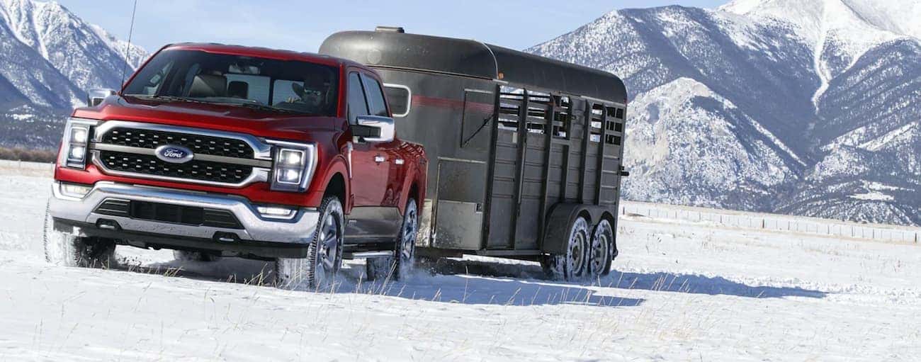 A red 2021 Ford F-150 Hybrid is towing a trailer in the snow.