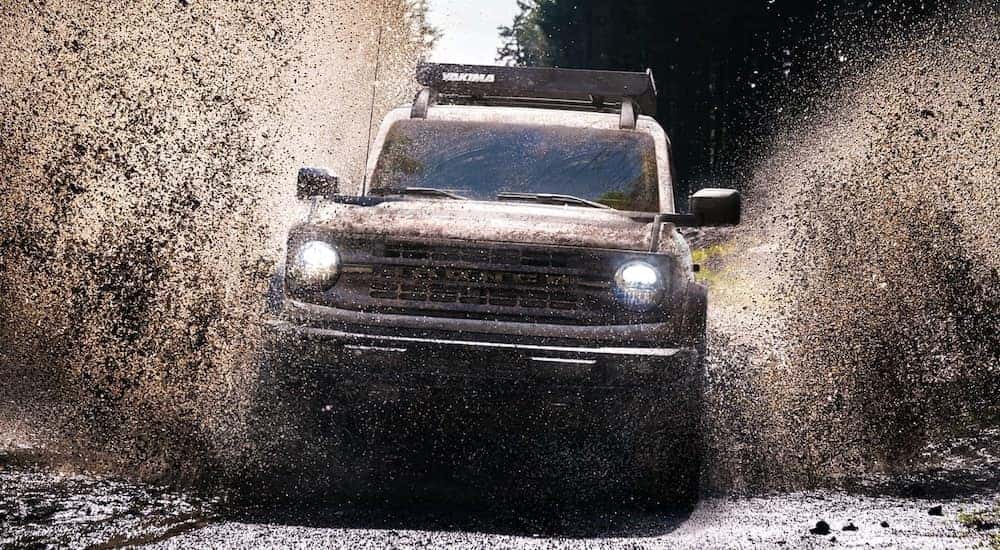 A silver 2021 Ford Bronco is splashing through a huge mud puddle.