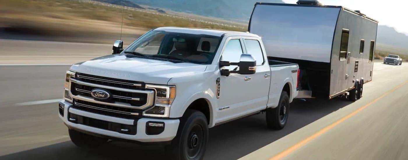 A popular Ford diesel truck, a white 2021 Ford F-350, is towing a trailer on an empty highway.