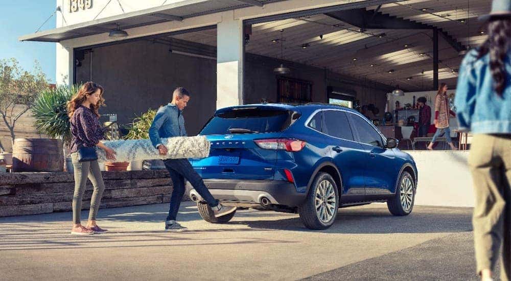 A couple is loading a rug into the rear of a blue 2021 Ford Escape.