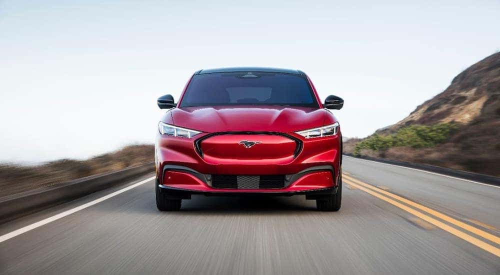 A red 2021 Ford Mustang Mach-E is shown from the front on a highway after leaving an Albany car dealer.