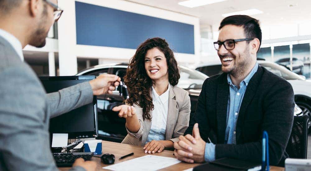 A salesman is handing keys to a happy couple at an Albany used car dealer.