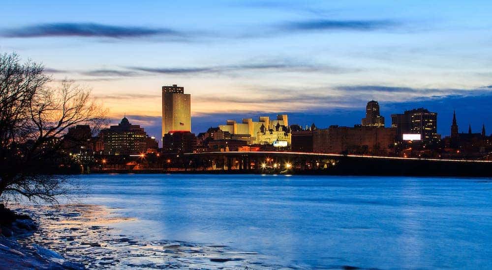 The Albany skyline is shown from across a river at dusk.