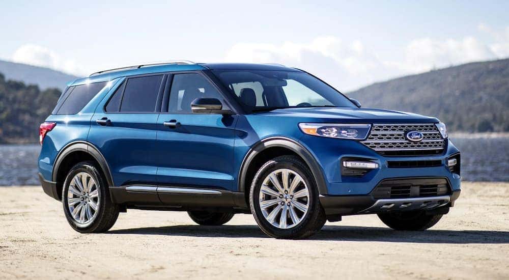 A blue 2021 Ford Explorer from a local Ford dealer is parked in front of a lake and hills.