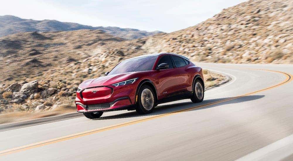 A red 2021 Ford Mustang Mach-E is driving on a desert highway.
