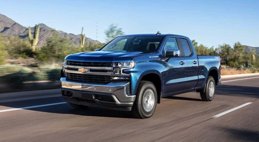 A blue 2019 Chevy Silverado is drivign on a road past desert shrubs and mountains.