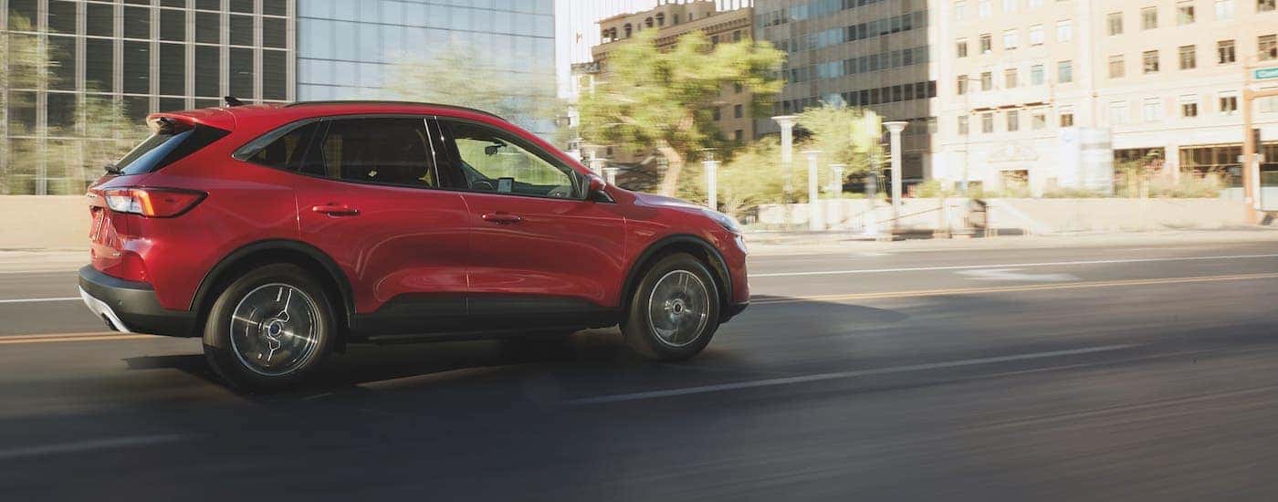 A red 2021 Ford Escape is driving on a city street and shown from the side.