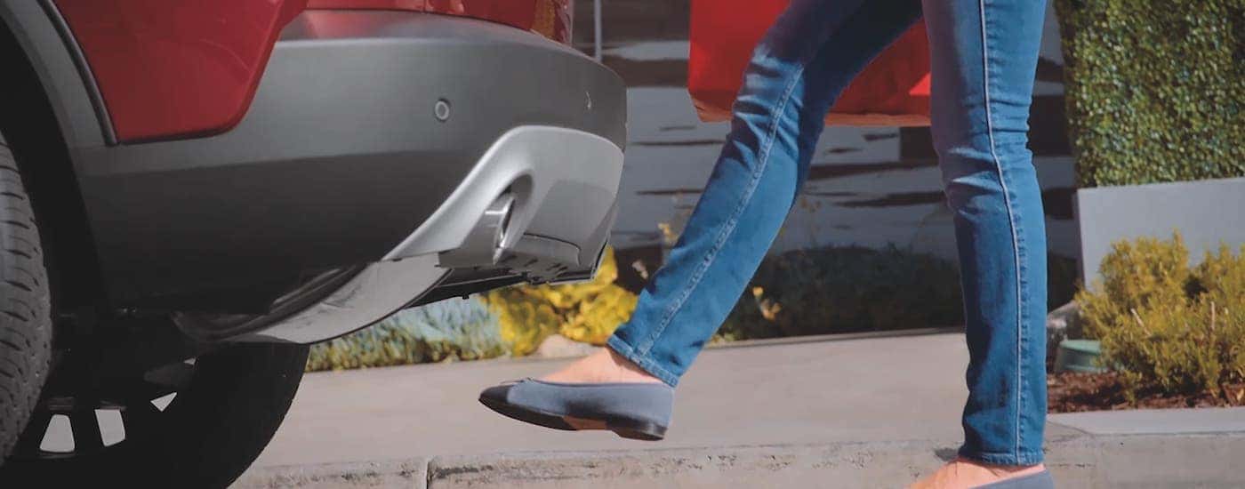 A closeup shows a foot waving under the rear of a red 2021 Ford Escape to open the liftgate.