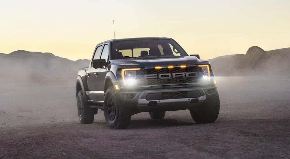 A black 2021 Ford Raptor is shown from the front at dusk with the headlights illumintaed.