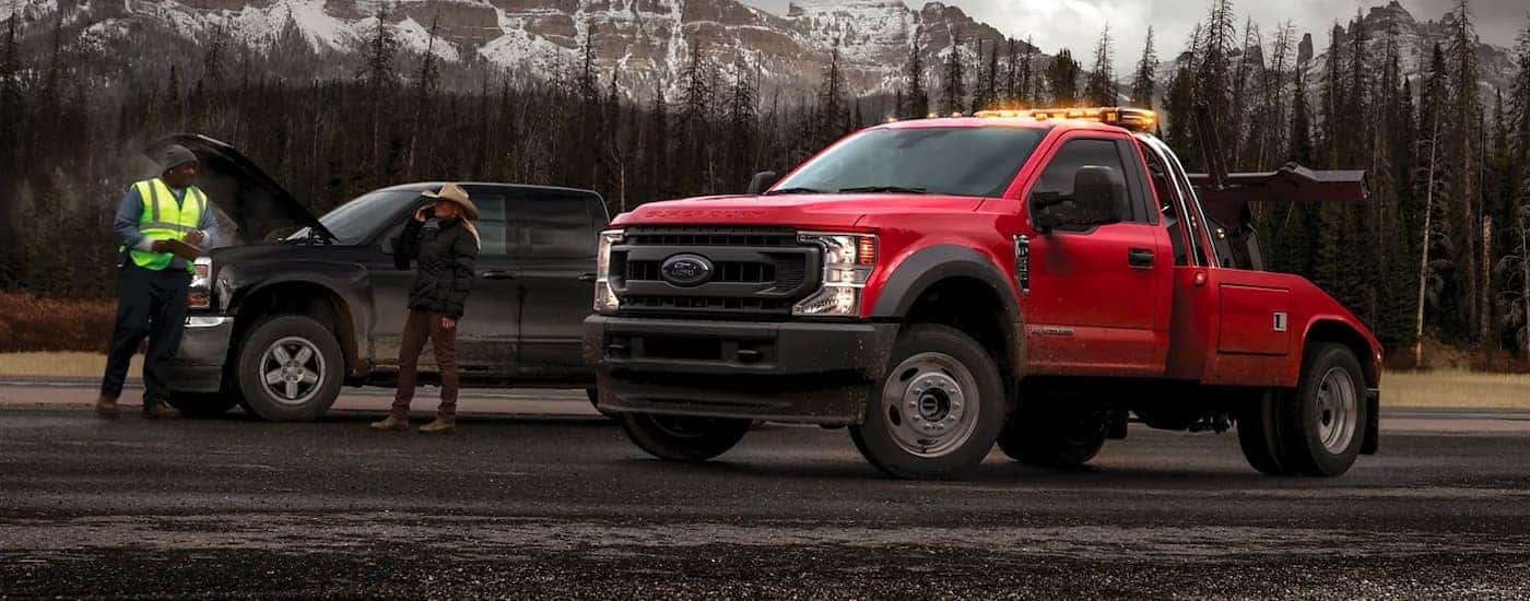 A red 2021 Ford Chassis Cab F-450 is shown from the side parked next to a broken down black truck.