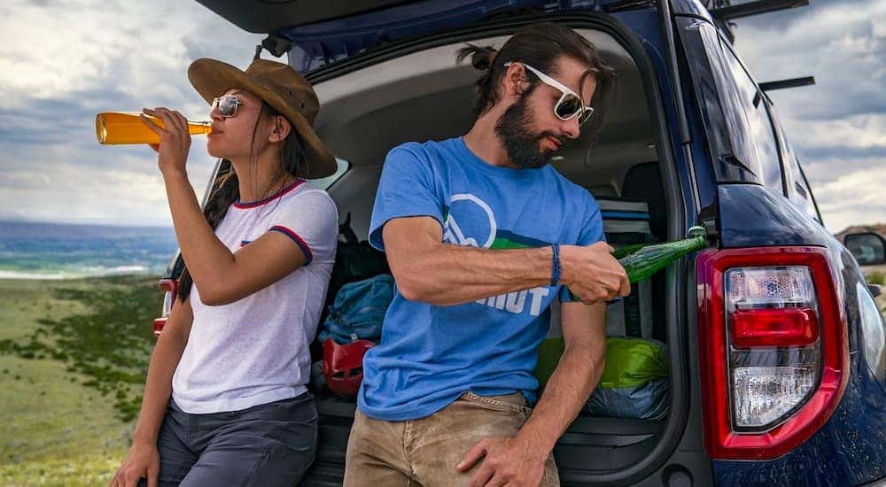 Two people are drinking beverages while leaning against a blue 2021 Ford Bronco Sport.