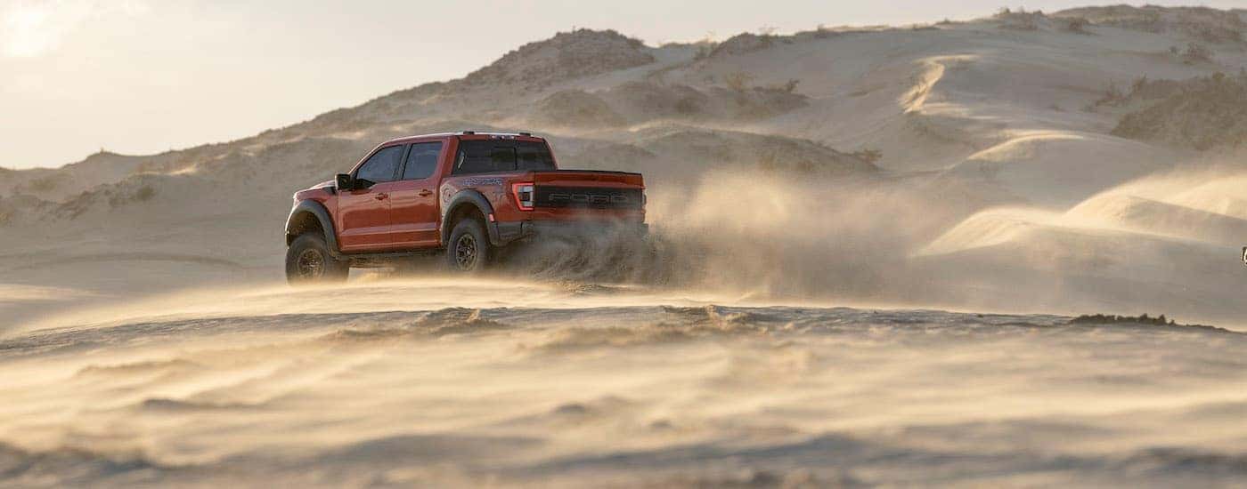 A red 2021 Ford F-150 Raptor is shown from the side driving through the dirt while kicking up dust.