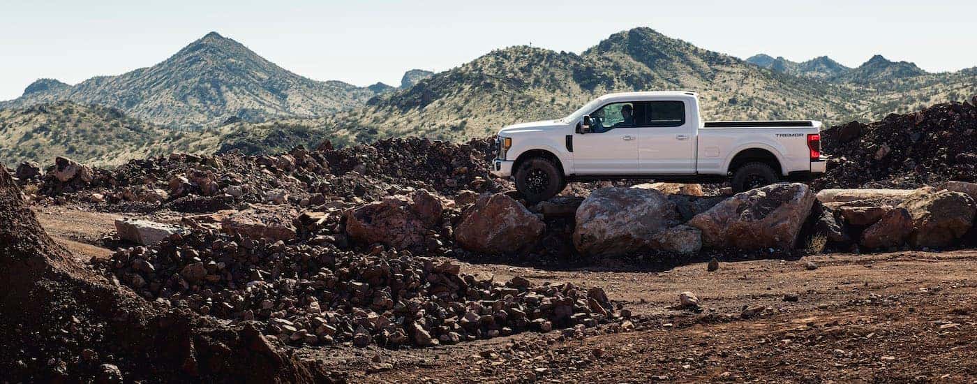 A white 2021 Ford F-250 Tremor Sport is parked on a dirt pile with mountains in the distance.