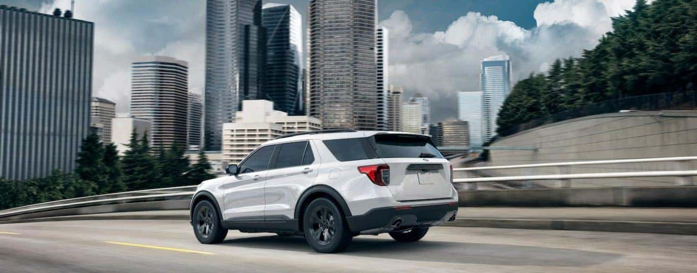 A white 2021 Ford Explorer is shown from the side driving past a city after winning the 2021 Ford Explorer vs 2021 Jeep Grand Cherokee comparison.