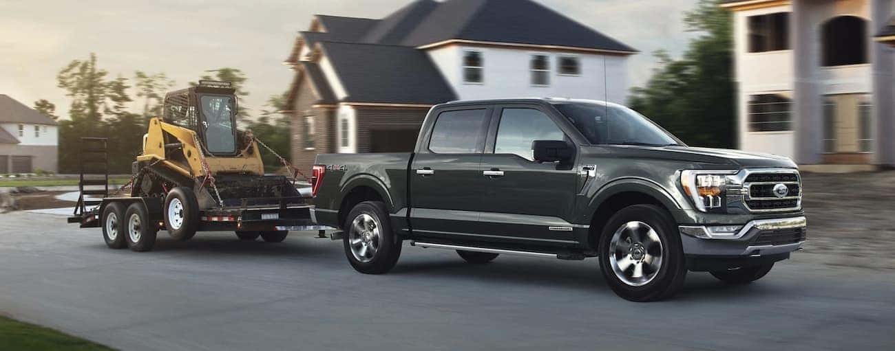 A dark grey 2021 Ford F-150 is towing machinery in a neighborhood development after winning the 2021 Ford F-150 vs 2021 GMC Sierra 1500 comparison.
