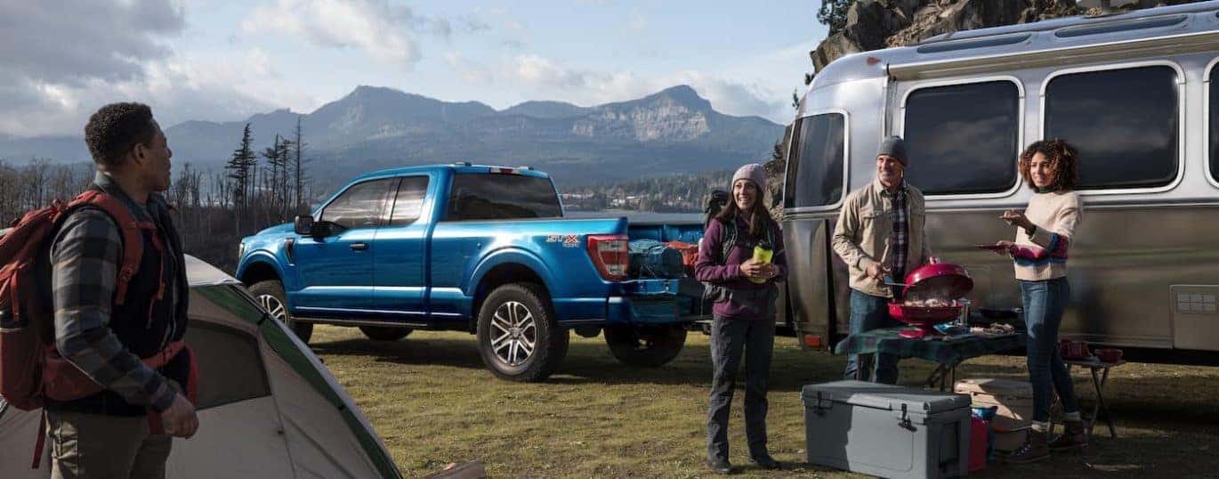 A blue 2021 Ford F-150 is shown from the side parked in the middle of a camping area.