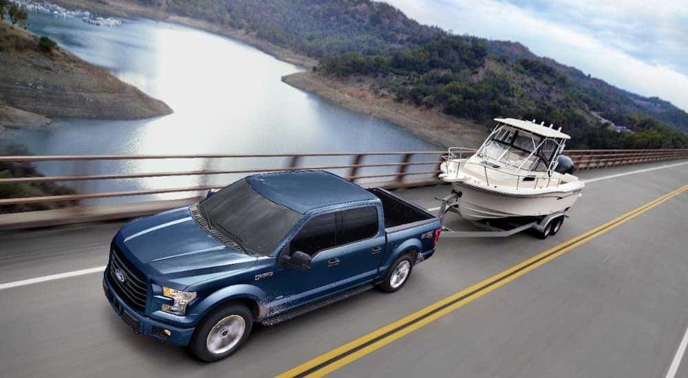 A blue 2017 Ford F-150 XLT is shown from a high angle towing a boat, on a bridge, over a river.