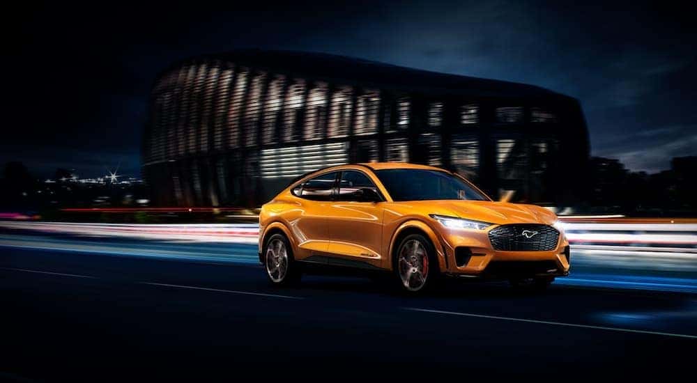 A yellow 2021 Ford Mustang Mach-E GT is driving through a city at night.