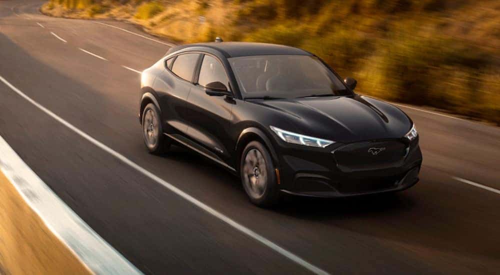 A black 2021 Ford Mustang Mach-E is driving at sunset.