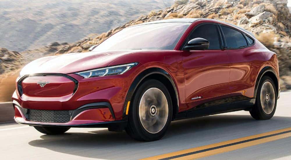 A red 2021 Ford Mustang Mach-E is driving down a two way road past the desert.