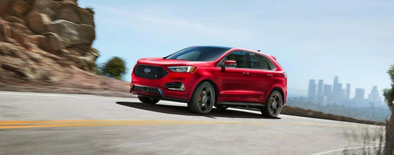 A red 2021 Ford Edge ST is shown driving down a road with a city in the distance.