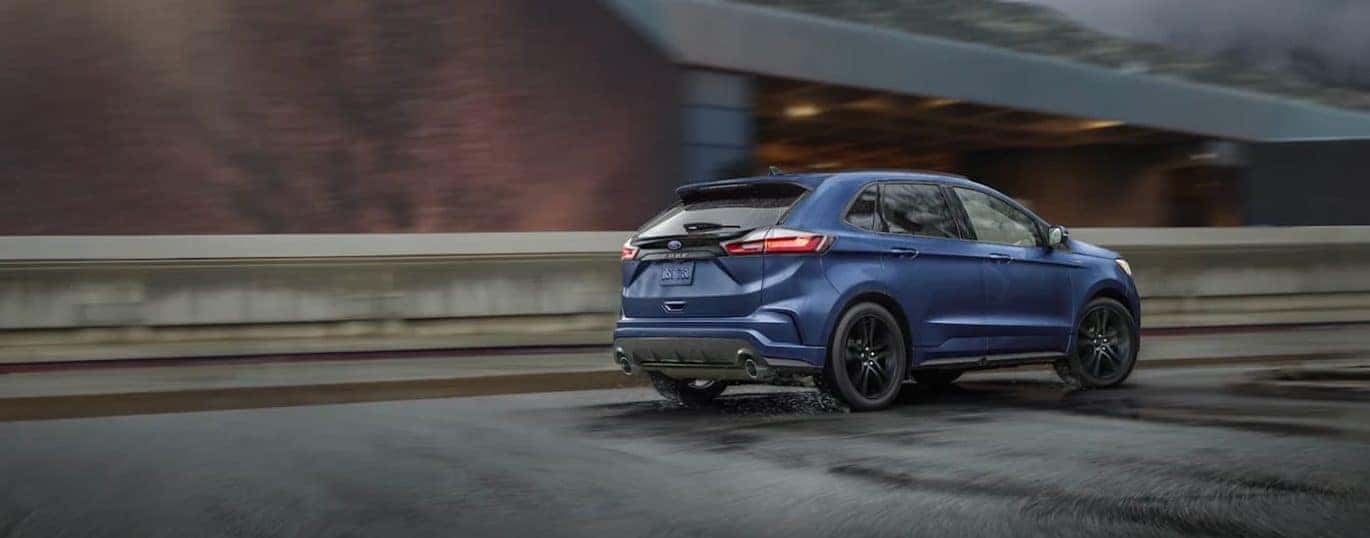 A blue 2021 Ford Edge ST is shown from the rear while driving down a road in the rain.