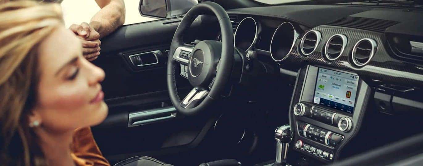 A close up shows a woman in the passanger seat and the black interior in a 2021 Ford Mustang.
