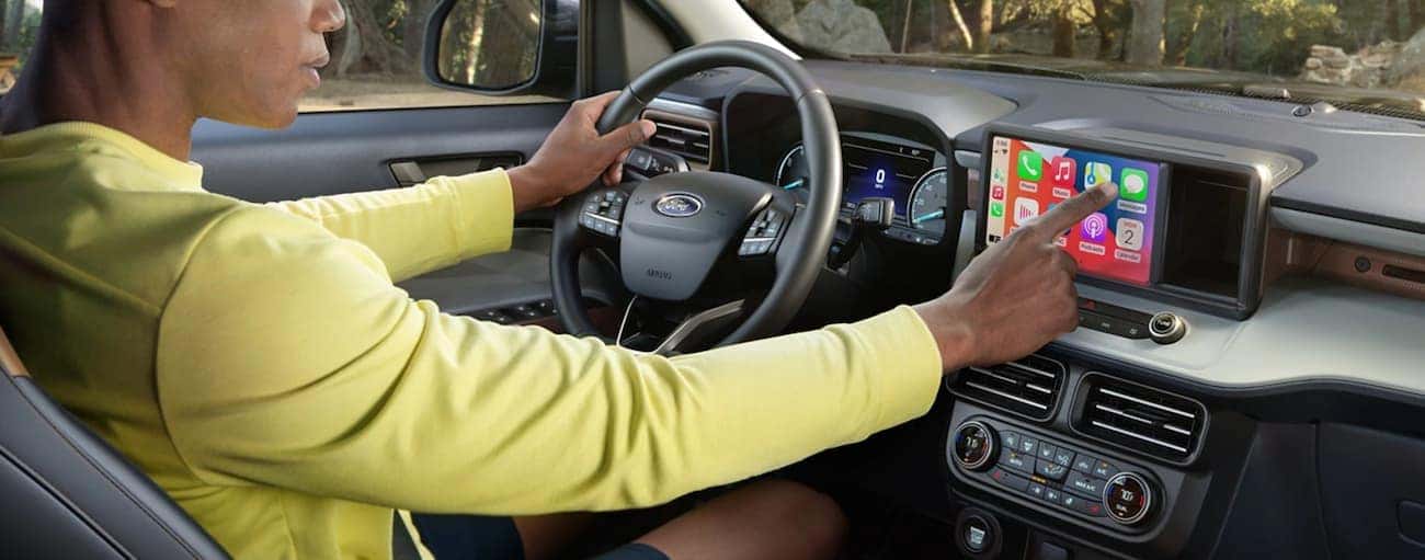 The interior of a 2022 Ford Maverick shows a man sitting in the drivers seat adjusting the infotainment screen.