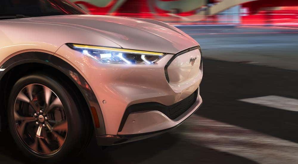 A white 2021 Ford Mustang Mach-E shows the front of the car driving through a city.