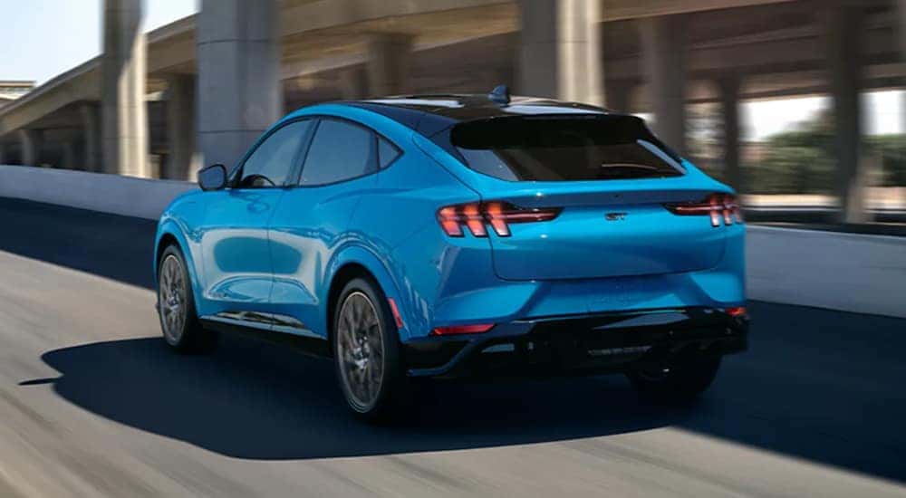 A blue 2021 Ford Mustang Mach-E is shown from the back driving up an on-ramp.