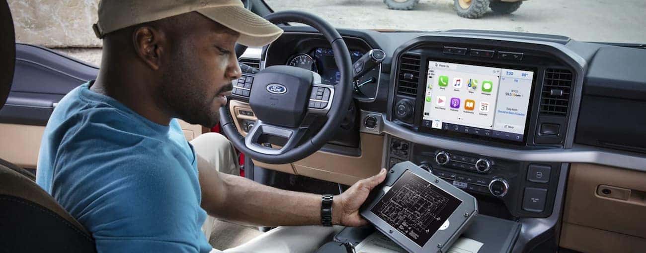 The interior of a 2021 Ford F-150 shows a man using a tablet in the front seat.